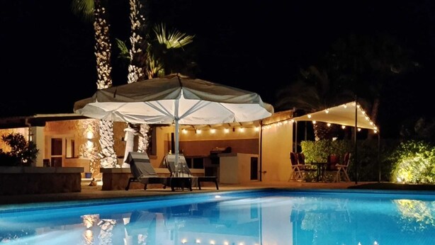 A swimming pool with lounge chairs and an umbrella, surrounded by a stone wall and palm trees. - Romantic finca with pool between Campos and Colonia Sant Jordi in the countryside (Campos)