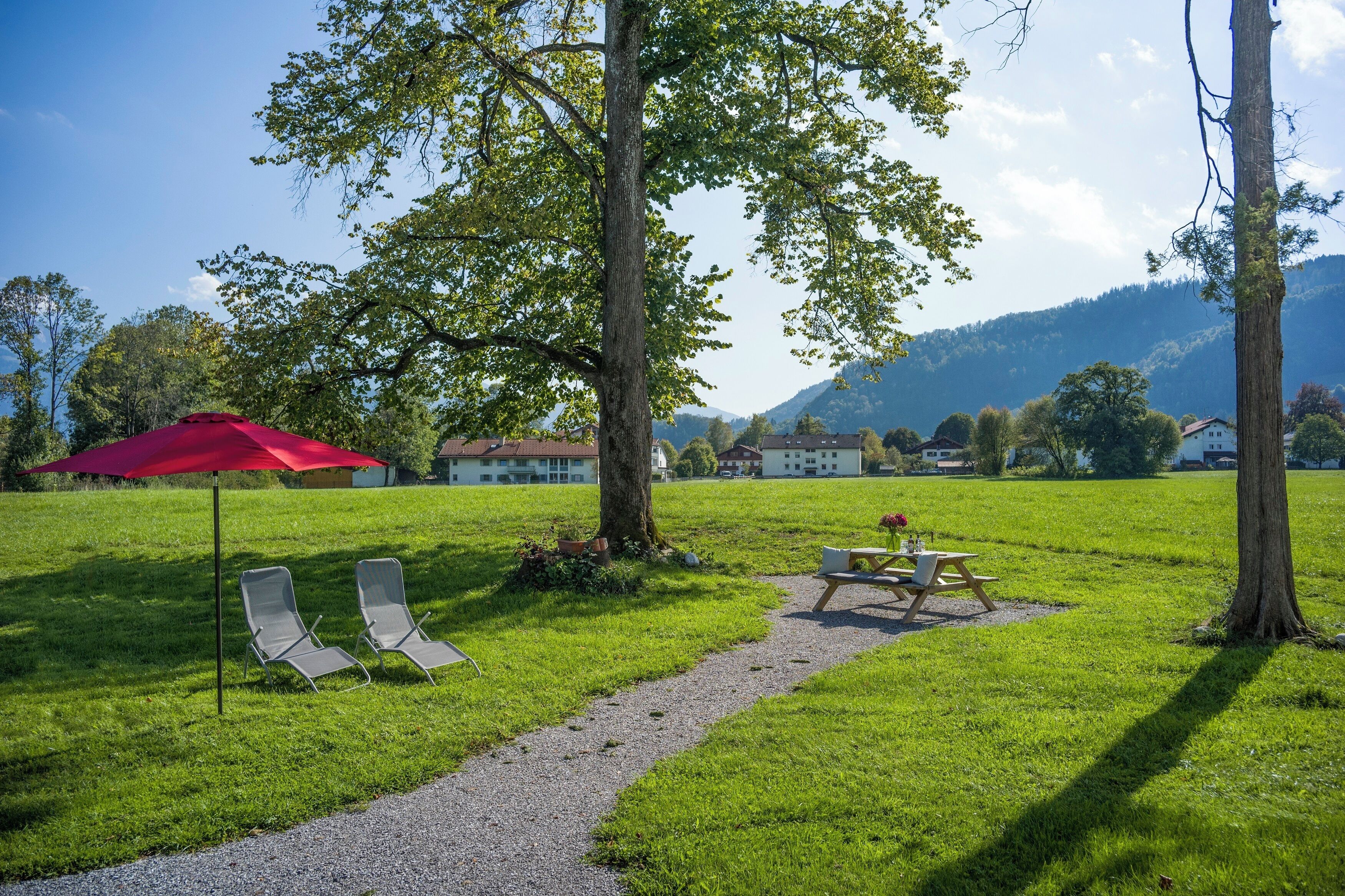 Un espacio al aire libre con césped, dos sillones de relax, una sombrilla roja, una mesa de picnic y un sendero de grava.