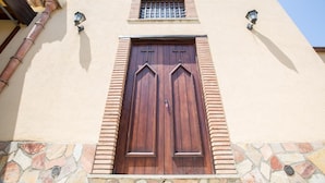 A building with a large wooden door, stone steps, and a small window with a metal grille. - La Casa Del Priore (Patti)