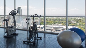 A gym with exercise equipment and large windows overlooking a cityscape.