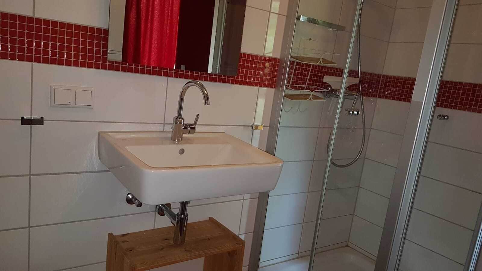 Une salle de bain avec un lavabo blanc, une serviette rouge et une cabine de douche en verre.