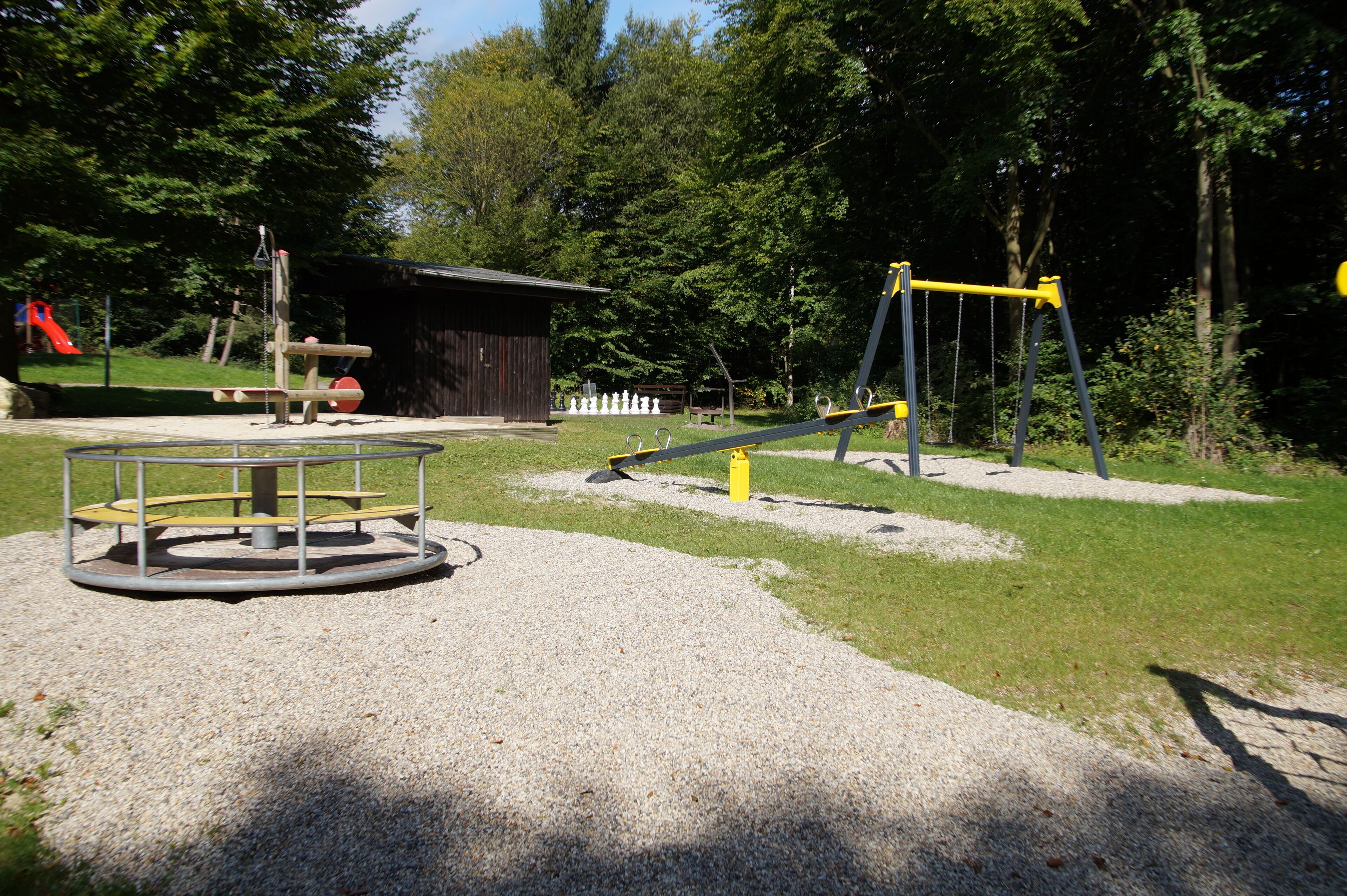 Ein Spielplatz mit Schaukel, Wippe und Karussell.