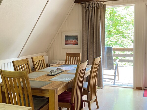 Un área de comedor con mesa y sillas de madera, vista a la vegetación exterior y un cuadro en la pared.