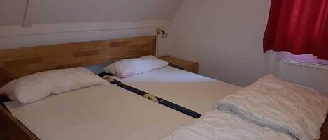 A single bed with a wooden headboard, white bedding, and a red curtain on the window.