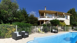 A two-story house with a swimming pool, surrounded by a fence and various outdoor furniture.