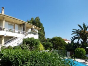 A two-story house with a balcony, a swimming pool, and lush greenery.