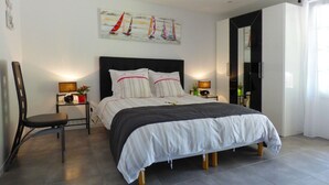 A modern bedroom with a large bed, two bedside tables with lamps, a chair, and a painting of sailboats on the wall.