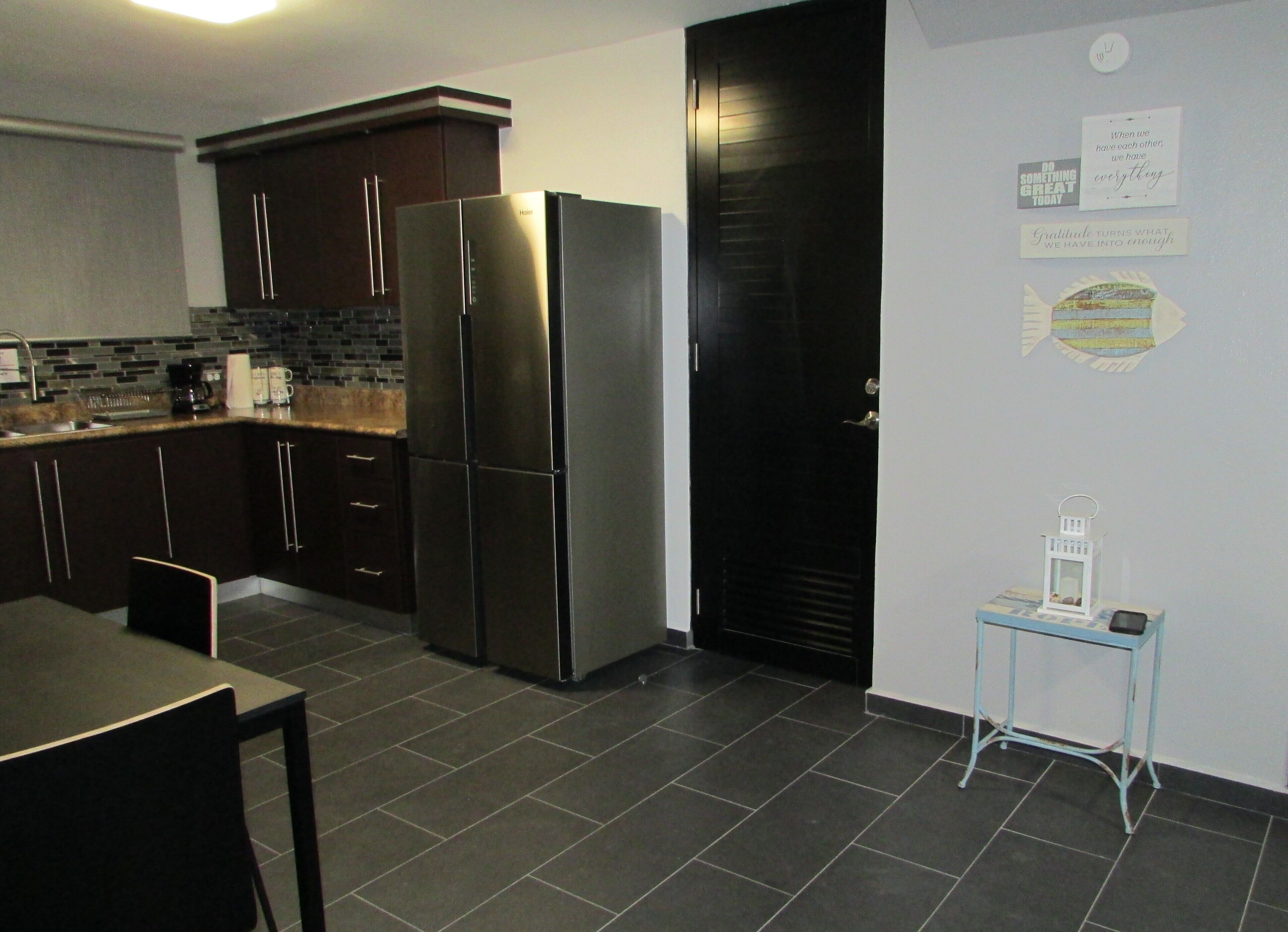 A modern kitchen with dark cabinetry, a stainless steel refrigerator, and a tiled floor.