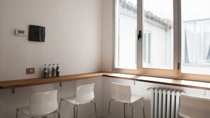 A corner room with a wooden shelf, two white chairs, a radiator, and a window with a view of a building outside. - La Sapienza Di Al (Siena)