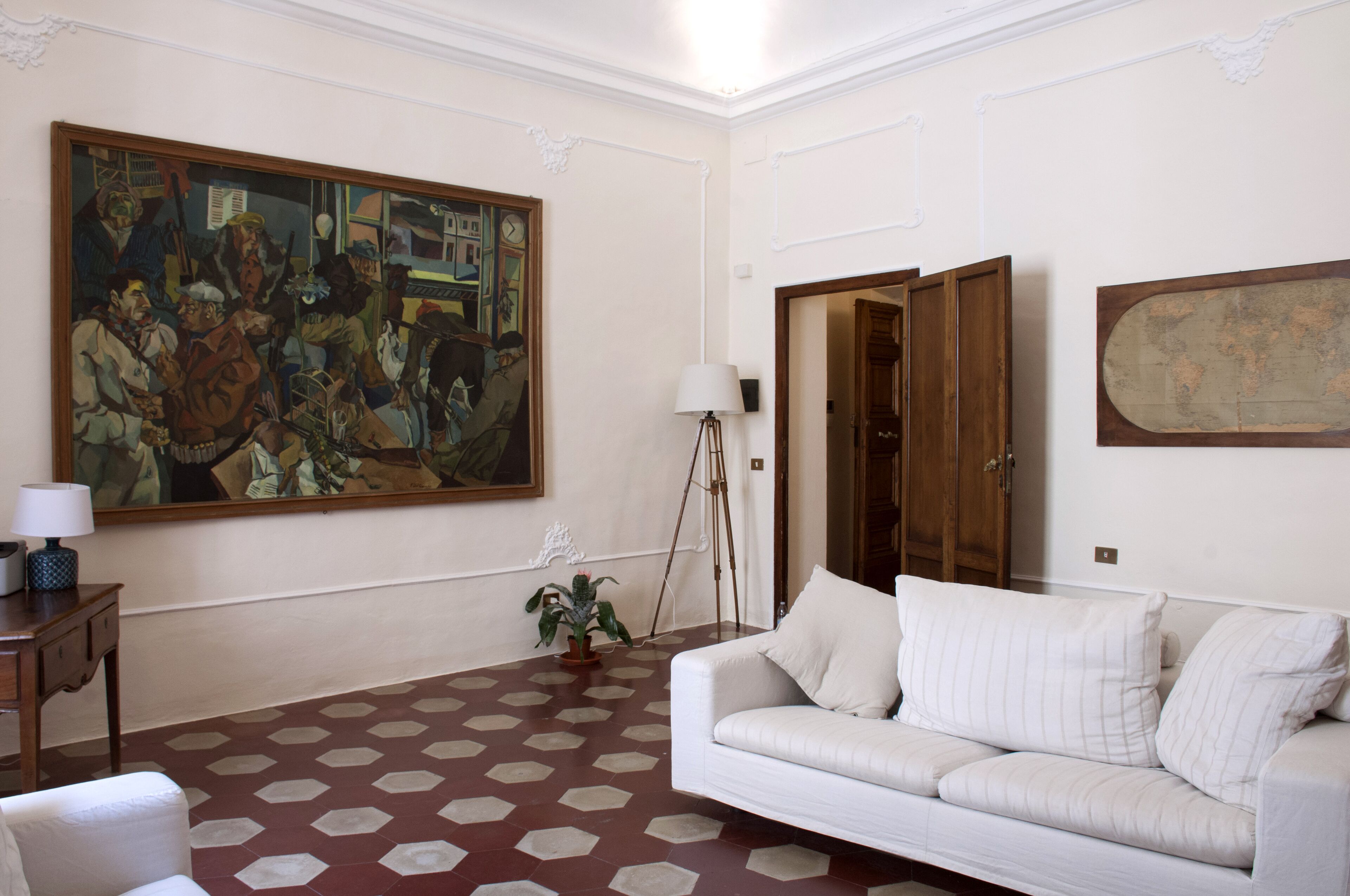 Un salon avec un grand tableau, un canapé blanc, un meuble en bois et un sol orné d’un motif géométrique.