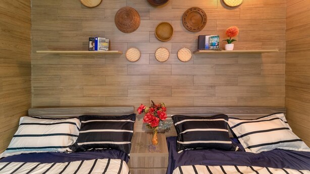 A room with two beds, a wall-mounted shelf with books and a potted plant, and a variety of woven baskets on the wall. - Hanoi Lotus Guest House (Hanoi)