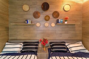 A room with two beds, a wall-mounted shelf with books and a potted plant, and a variety of woven baskets on the wall. - Hanoi Lotus Guest House (Hanoi)