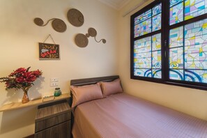 A bedroom with a bed, a nightstand, a vase with flowers, a wall decoration, and a window with stained glass. - Hanoi Lotus Guest House (Hanoi)