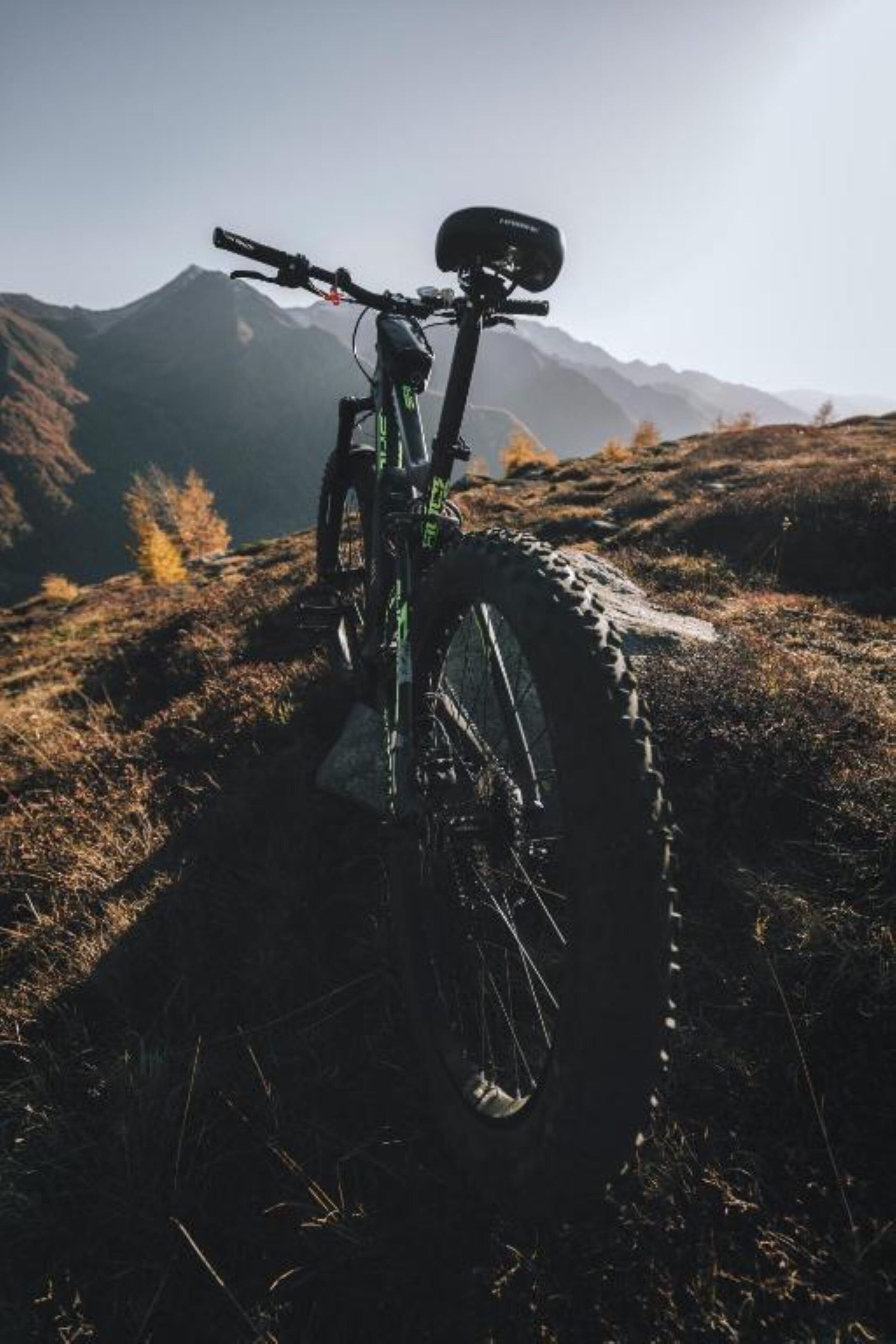 Una bicicleta de montaña aparcada en una ladera cubierta de hierba, con montañas al fondo.