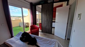 Ein Hotelzimmer mit Bett, einem roten Sessel und Blick auf einen Garten sowie ein Gebäude.