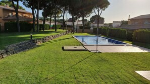 A well-maintained pool area with a stone border, surrounded by neatly trimmed grass and trees.