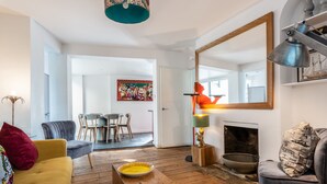 A living room with a wooden floor, a yellow sofa, a grey armchair, a wooden coffee table, a fireplace, and a large mirror. - Birch at Ship St Gardens (Brighton)