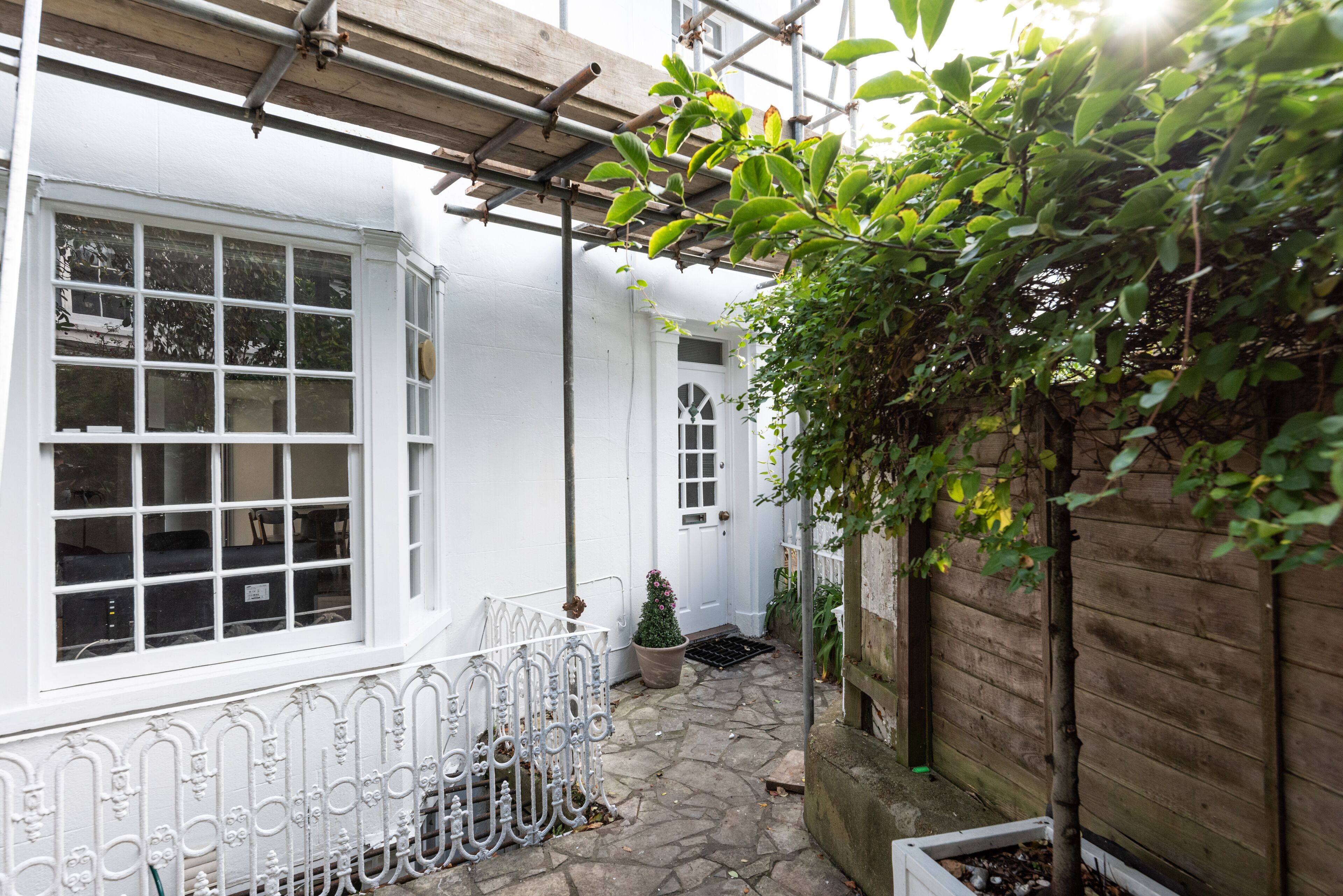 A narrow stone pathway leading to a white building with a wooden fence and a metal gate.