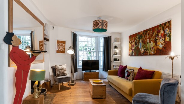 A living room with a wooden floor, a yellow sofa, a blue armchair, a TV, and a large painting on the wall. - Birch at Ship St Gardens (Brighton)