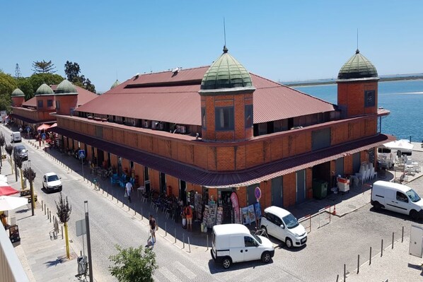 A large brick building with a red roof and green domes, featuring a covered outdoor seating area and a view of the water. - 100 m2 apartment in Olhão, central, for rent. (Olhão)