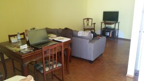A living room with a sofa, a wooden table with a laptop, a chair, and a television on a stand. - 100 m2 apartment in Olhão, central, for rent. (Olhão)