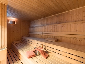 A sauna with wooden benches and a bench seat, a towel, and a metal bucket. - Holiday Resort Oberaudorf 2 room apartment F2 (Oberaudorf)