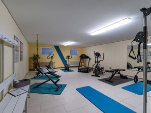 Een sportschool met trainingsapparatuur, blauwe matten en een witte vloer.