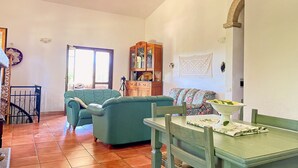 A living room with a sofa, a dining table with chairs, a wooden cabinet, and a window.
