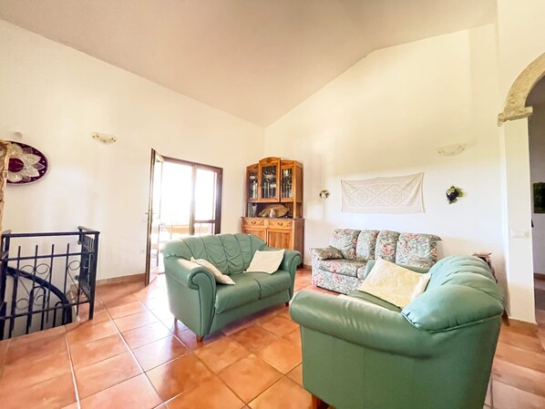 A living room with two green sofas, a wooden cabinet, and a tiled floor. - VILLA in the countryside in Sardinia (TEMPIO PAUSANIA)