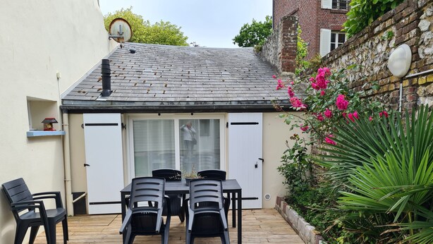A patio with a table and chairs, a white door, and a brick wall with plants.