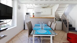 A dining area with a table set for four, a television on the left, and a kitchen in the background.