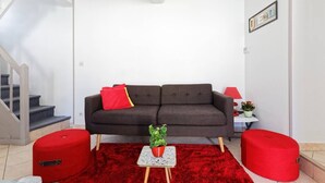 A modern living room with a grey sofa, red cushions, a small table with a plant, and red ottomans.