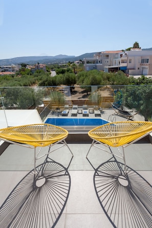 Terraço no telhado com piscina, duas cadeiras de vime amarelas e guarda-corpo de vidro.