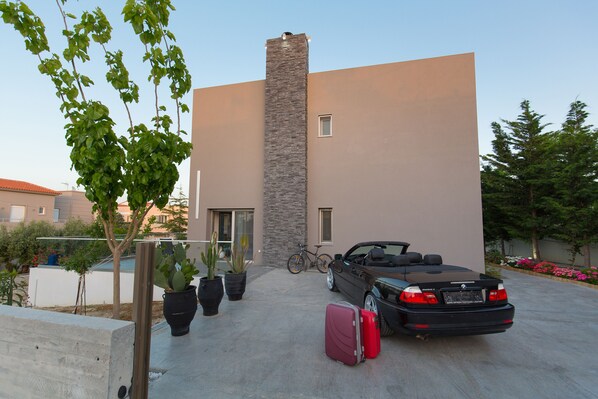 A modern building with a stone facade, a parked convertible, and a suitcase on the driveway. - Villa Kastellakia (Rethymno)