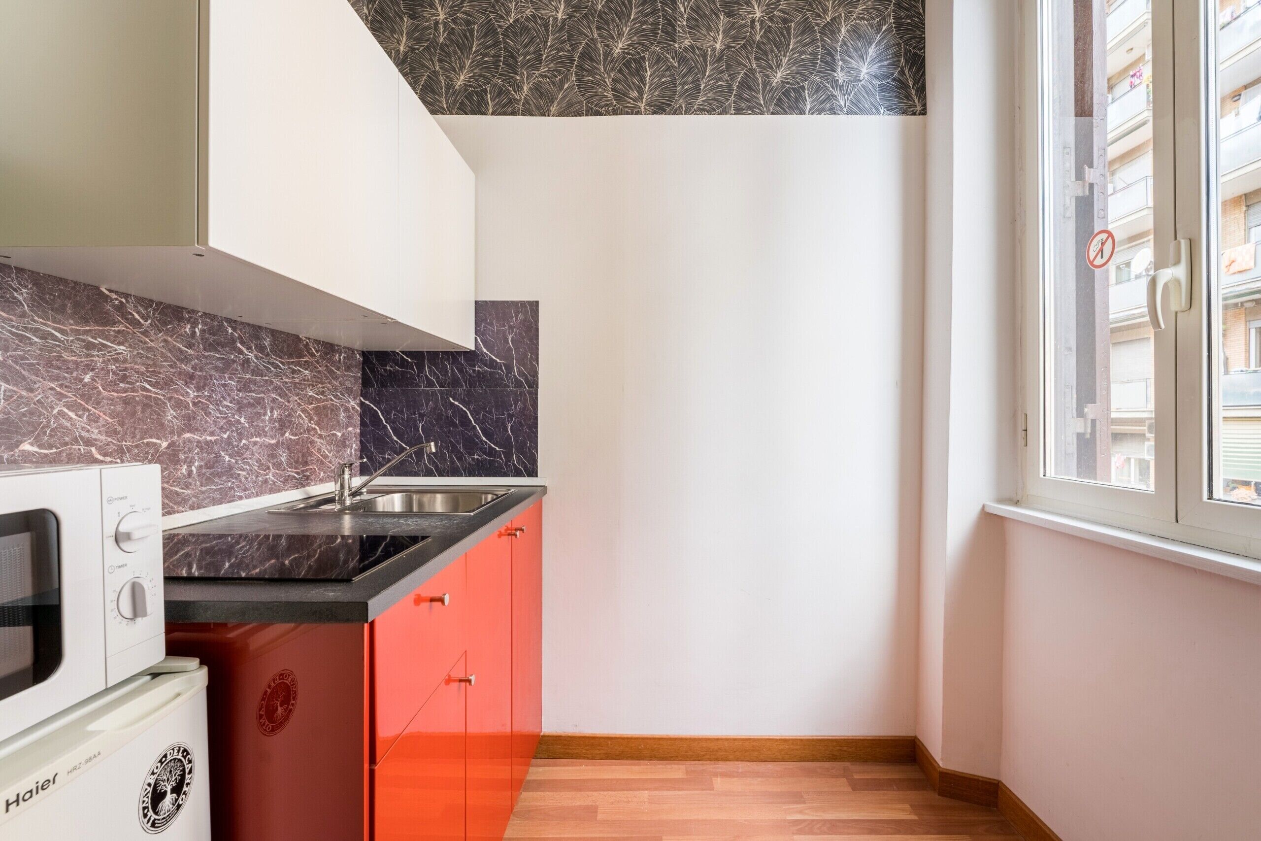 Una cocina compacta con encimera negra, horno integrado y un armario rojo.