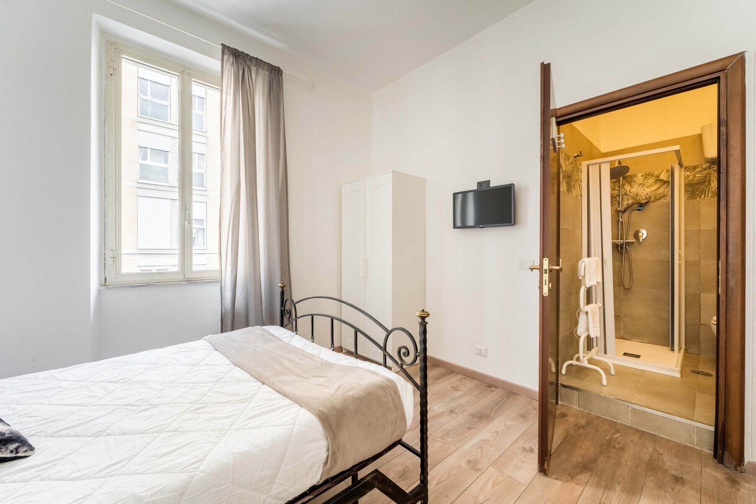 Una camera da letto con un letto, una finestra con tende, un armadio e un angolo doccia con porta in vetro.