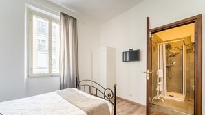 A bedroom with a bed, a window with curtains, a wardrobe, and a shower area with a glass door. - Rooms Piramide (Rome)
