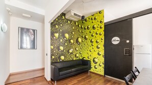 A modern interior with a black sofa, a wooden floor, a green wall with bubble patterns, a 'Welcome' sign, and a dining area with chairs and a table. - Rooms Piramide (Rome)