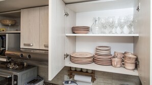 Una cocina con horno empotrado, tostadora y microondas. Hay estantes con platos, tazones y tazas.