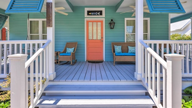 A porch with a red door, two wicker chairs with blue cushions, and a ceiling fan. - Cottage w/ Porch - 3 Min Walk to Bay St Louis (Bay St. Louis)