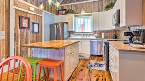 A kitchen with wooden paneling, a stainless steel refrigerator, white cabinets, and a wooden island with stools. - Cottage w/ Porch - 3 Min Walk to Bay St Louis (Bay St. Louis)