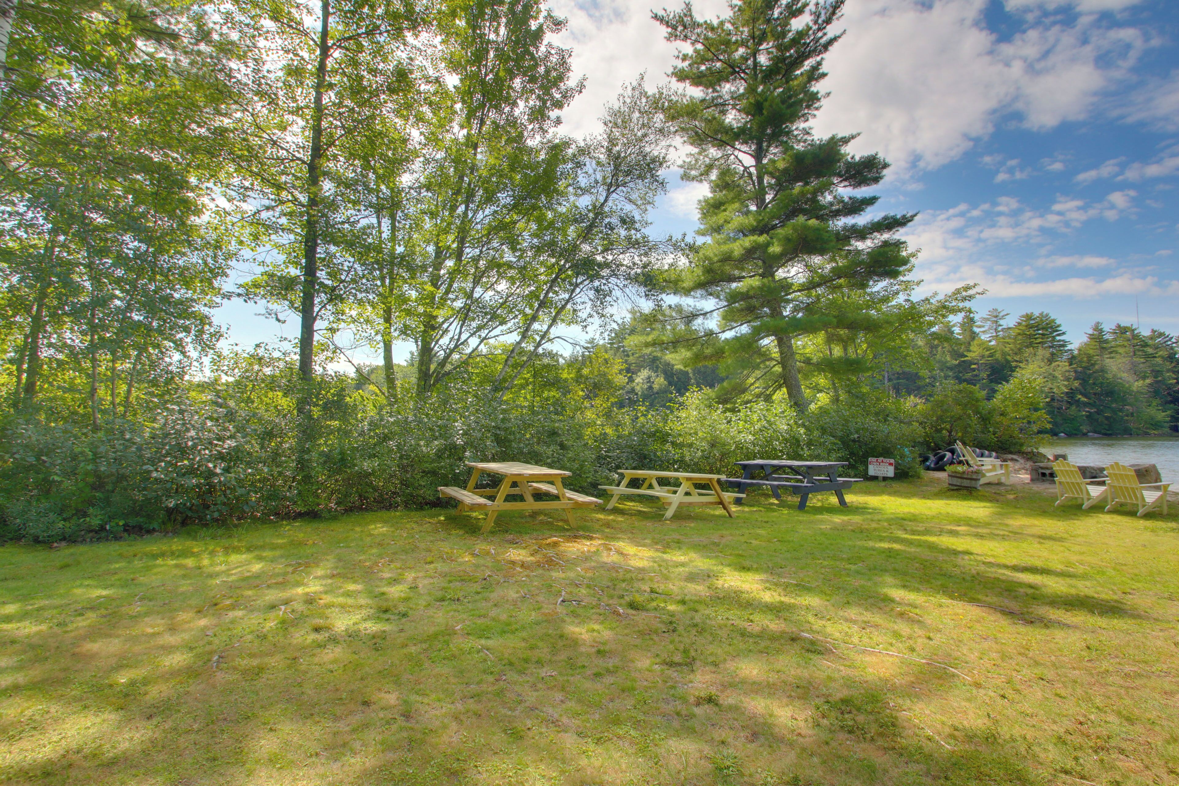 A picnic area with picnic tables and chairs, surrounded by trees and a lake.