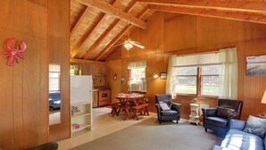 Ein gemütliches Blockhauskamin-Interieur mit Holzvertäfelung, einem Esstisch, zwei Stühlen, einer Couch und einem Deckenventilator.