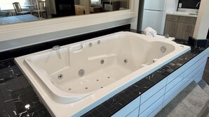 Un baño moderno con una bañera grande, un espejo y vistas a la cocina y la sala de estar.