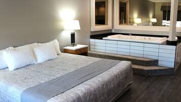 Una habitación de hotel con una cama grande, un baño con bañera y un espejo sobre el lavabo.
