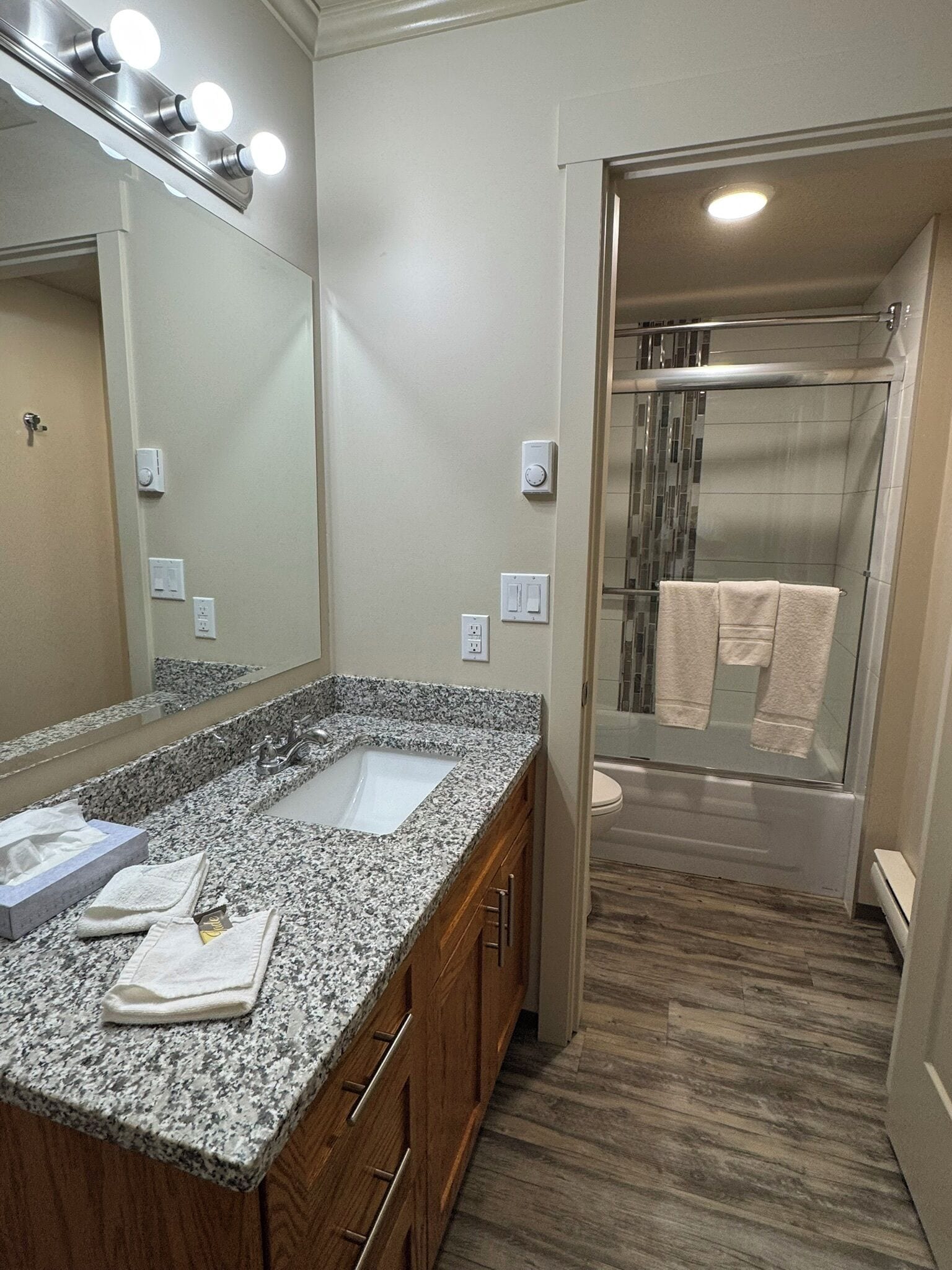 A bathroom with a granite countertop, a large mirror, and a shower with a glass door.