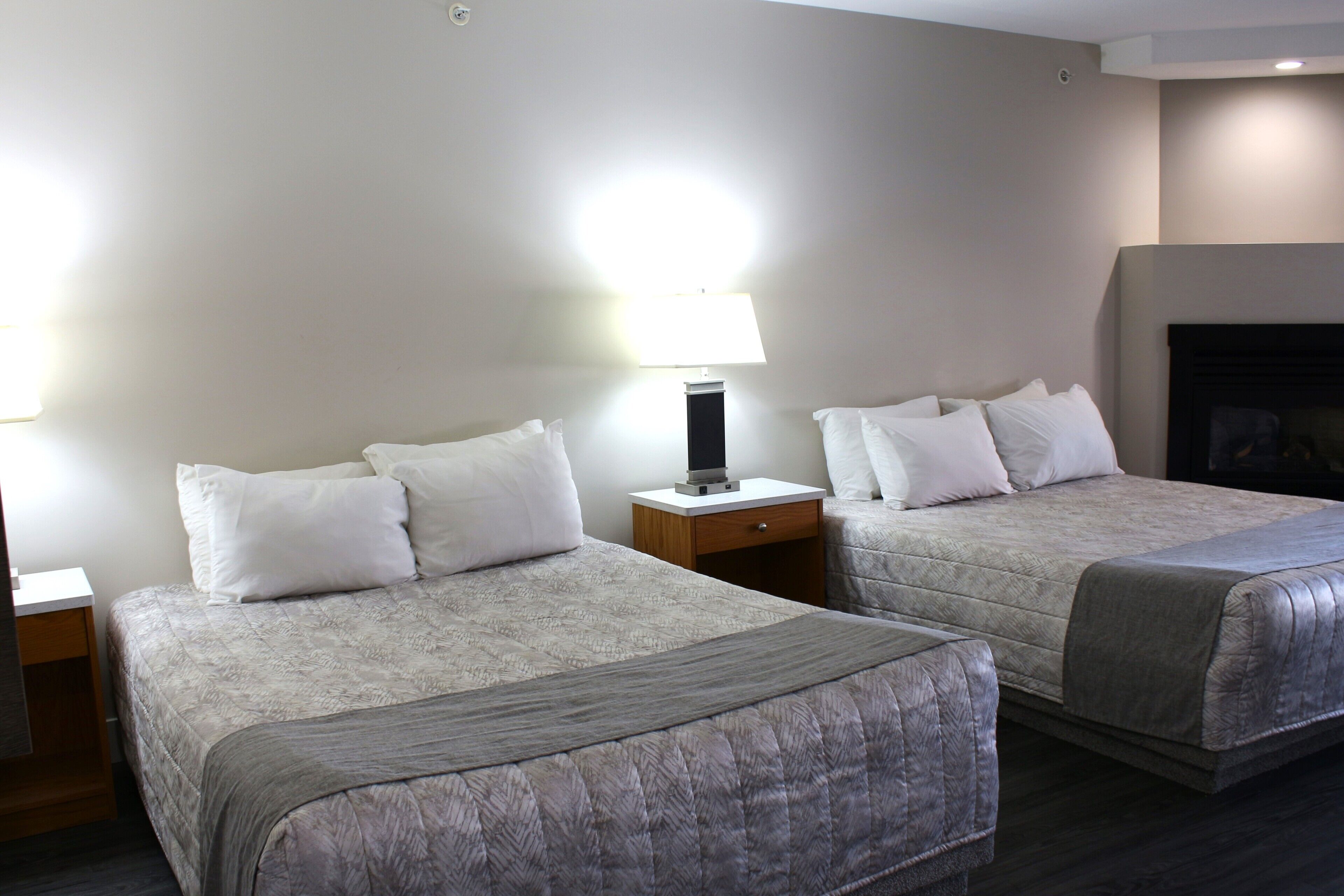 Une chambre d’hôtel avec deux lits, une table de chevet avec une lampe et une cheminée.