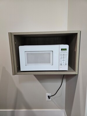 Forno de micro-ondas fixado numa prateleira de madeira acima de uma tomada na parede.