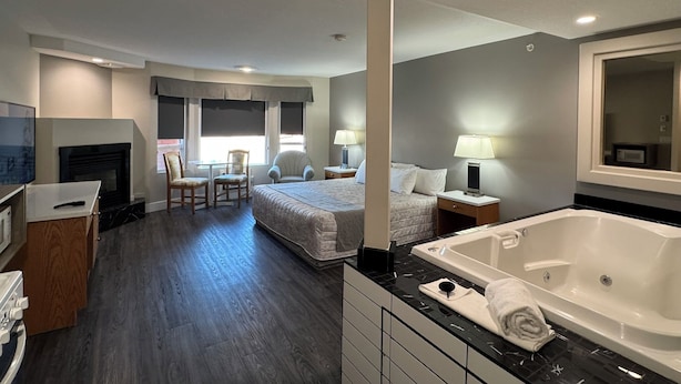 Una habitación de hotel con una cama grande, una zona de estar separada con una silla y una mesa, una chimenea, una bañera y un televisor.