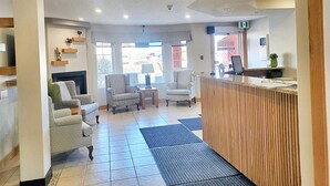 Un vestíbulo de hotel con mostrador de recepción, zona de estar con sillones, chimenea y grandes ventanales.